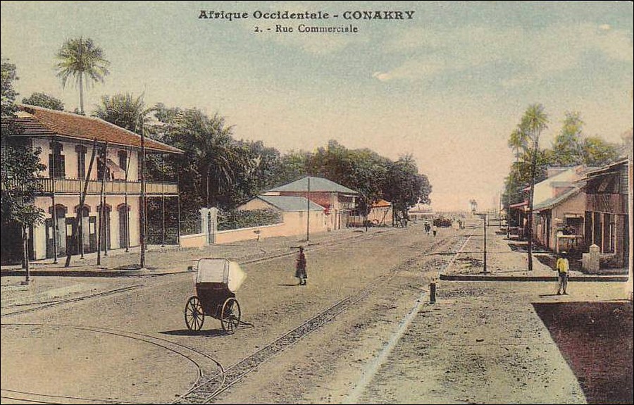 la rue commerciale à Conakry, avec un pousse-pousse stationné en travers et des rails type Decauville courant au sol